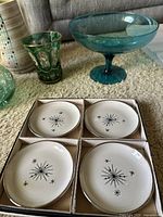 Close-up view of set of four white porcelain saucers with black starburst mid-century modern design arranged in cardboard holder