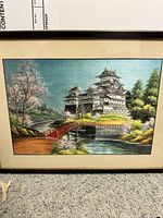 Framed Japanese silk embroidery showing a castle with a red bridge and cherry blossom trees