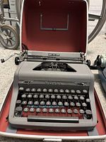 Gray manual Royal Quiet De Luxe typewriter inside open red-lined case, showing keyboard and brand plate