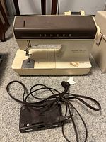 Singer Fashion Machine 1030 sewing machine showing front and side profile. Cream body with brown top panel, the Singer brand name in metallic letters on front.