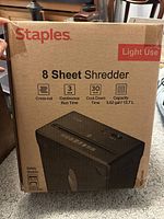 Front view of the boxed Staples 8-sheet shredder indicating cross-cut shredding, continuous runtime, cool-down time, and bin capacity, marked for light use.