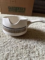 Side view of beige ceramic gravy boat showing linear decorative band and handle on carpeted surface.