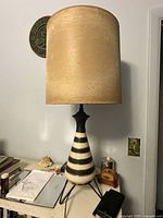Full view of the vintage lamp showing beige fabric shade and striped ceramic base on tripod stand.
