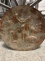 Full view of the round copper piece with hammering and embossed folk art images of animals and celestial symbols.