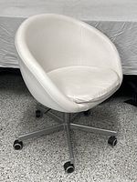 Front and side view of the IKEA SKRUVSTA swivel chair showing white vinyl upholstery, bucket seat design, removable cushion, and five-wheel metal base.