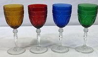 Four Luminarc goblets in amber, red, blue, and emerald green lined up side by side showing full height and pattern details