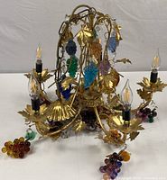 Overview of the entire chandelier showing gold metal vine design, bubble shaped colored glass grapes hanging from vines, candle bulb sockets with LED bulbs installed.