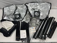 Photo showing two tungsten light heads, reflector soft boxes with silver lining and diffusers, multiple light stand rods, and owner's manual arranged together.