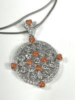 Close-up of circular pendant showing clear crystals and orange heart-shaped stones on sterling silver.