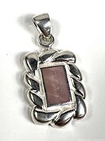 Front view of rectangular pink stone inlay pendant with silver twisted rope design frame.