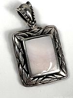 Front view of rectangular sterling silver pendant showing textured frame and light-colored inlay.