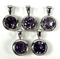 Top view of five sterling silver round pendants with faceted purple crystals arranged in a horizontal group on a white background.