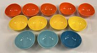 Top-down view of the 12 bowls in four colors (orange, yellow, light blue, dark blue) arranged in rows on a plain surface.