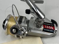 Close-up image of the fishing reel from the left side showing the spool with line, model label, gear ratio, and metal construction.
