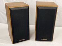 Pair of vintage Polk Audio bookshelf speakers with wood veneer cabinets and black fabric grill cloth, showing front and side angles.