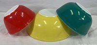 Three Pyrex mixing bowls inverted showing red, yellow, and teal colors