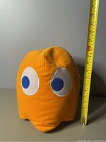 Front view of the orange Clyde plush with a measuring tape showing a height of about 12 inches.