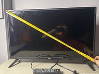 32-inch RCA TV with a measuring tape held diagonally across the screen showing size.