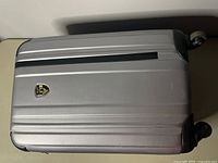 Front view of silver hard shell suitcase showing branded badge and textured surface.