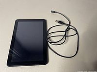 Amazon Fire 8 tablet front view with screen off and USB-C charging cable beside it