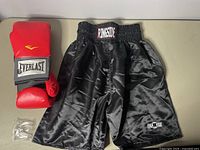 Photo showing Everlast red boxing gloves, black Ringside boxing shorts, and sealed mouthguard on table