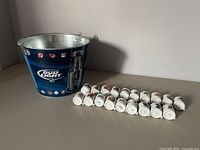 Blue Bud Light metal bucket with NHL team logos and some of the 24 novelty cups arranged in front.