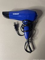 Side view of blue Conair hair dryer showing brand name, concentrator nozzle, power cord wrapped around handle.