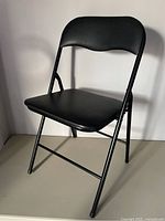 Side view of black folding chair showing padded seat and backrest with metal frame.