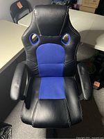Front view showing the black and blue gaming chair with padded armrests and seat with blue fabric insert.