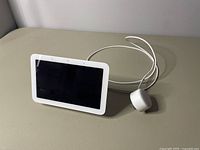 Front view of Google Nest Hub smart display with screen off and power adapter.