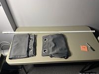 Two folded grey blackout curtains with metal grommets and one white curtain rod laid on a surface.