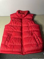 Front view of large red Old Navy sleeveless puffer jacket, showing high collar, front zipper, horizontal quilting and zippered pockets.