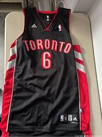 Front of black Toronto Raptors basketball jersey with "TORONTO" and number 6, Adidas and NBA logos visible.