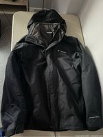 Full view of black Columbia Omni-Tech men's jacket laid flat showing front with zipper and hood