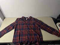 Full front view of men's medium Levi's plaid button-up shirt laid flat showing plaid pattern with red, navy blue, orange colors, long sleeves, and collar.