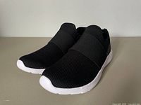 Front angled view of black slip-on running shoe with white sole showing mesh fabric upper and elastic midfoot band.