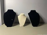 Front view of three necklace stands: two black velvet-textured and one white textured stand in the center.