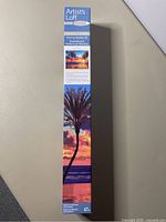 Photo of the sealed narrow box showing the painted sunset scene with palm trees and ocean reflection for the paint-by-number kit.