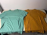 Photo showing two Old Navy men's large t-shirts, one teal green and one mustard yellow, laid out flat.