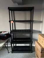 Full view of the black plastic storage shelf unit showing the five shelves and supporting posts.