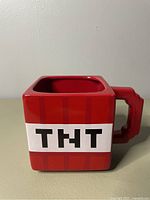 Side view of square red ceramic Minecraft TNT cup with blocky handle, showing ‘TNT’ in black on white band on side.