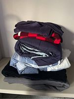 Stack of six folded blankets showing variety of colors and styles including red and navy, light blue striped, and solid navy.