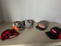 Lot of five hats arranged in a row showing different brands and styles.