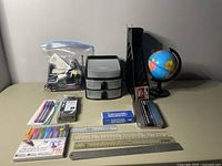Photo of all office supplies arranged on a table including globe, organizers, rulers, pens, pencil case, and small items in a ziplock bag