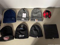 All various toques, neck warmer, and ear covers laid out on white surface showing different brands and colors