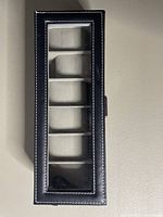 Top view of black watch holder box with five padded compartments under glass.