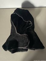 Front view of the black leather welding hood showing the hood opening and the extended flap with visible stitched edges for neck protection.