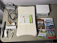 Full lot contents showing Wii console, cables, sensor bar, controllers, balance board, and Wii games.