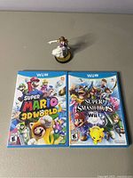 Front view of two Wii U game cases Super Mario 3D World and Super Smash Bros with Zelda Amiibo figure.