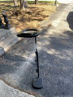 Full view of black floor lamp with adjustable height and oval base on asphalt ground.